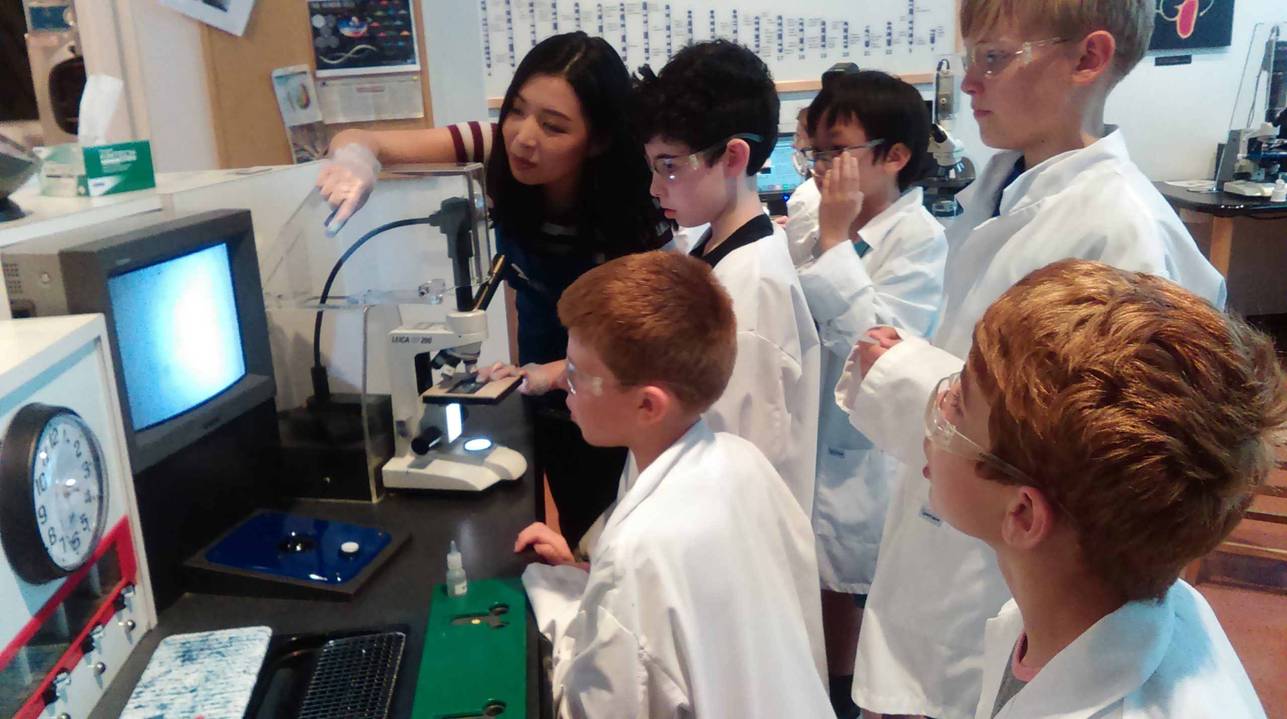 Explor Physics 4 ExplorSchool students and teacher looking at a microscope magnification